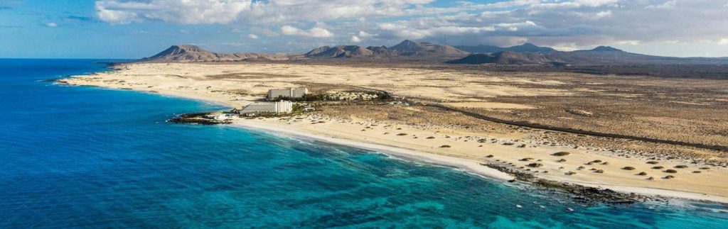 Vista aérea de las Grandes Playas de Corralejo en Fuerteventura, con dunas doradas, aguas turquesas y montañas volcánicas al