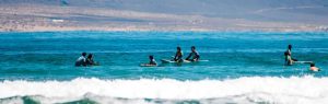 Clases de surf en la Playa de Famara, Lanzarote, con surfistas en el océano y montañas al fondo