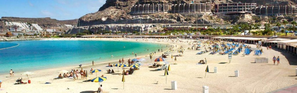 Playa de Amadores en Gran Canaria, con aguas turquesas, arena blanca y tumbonas bajo sombrillas de colores