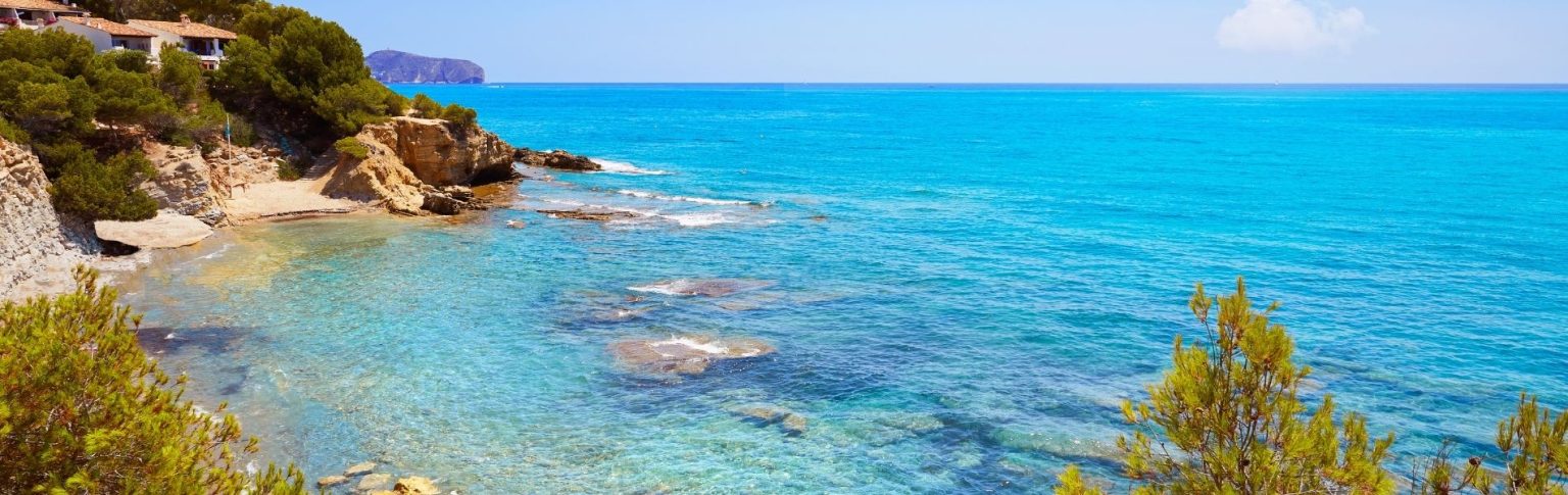 Cala transparente de Benissa con aguas turquesas cristalinas, rocas y vegetación mediterránea en la Costa Blanca