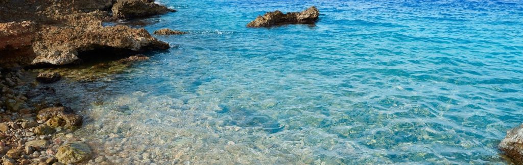 Aguas cristalinas turquesa de la costa rocosa de Dénia con piedras visibles bajo el mar transparente del Mediterráneo