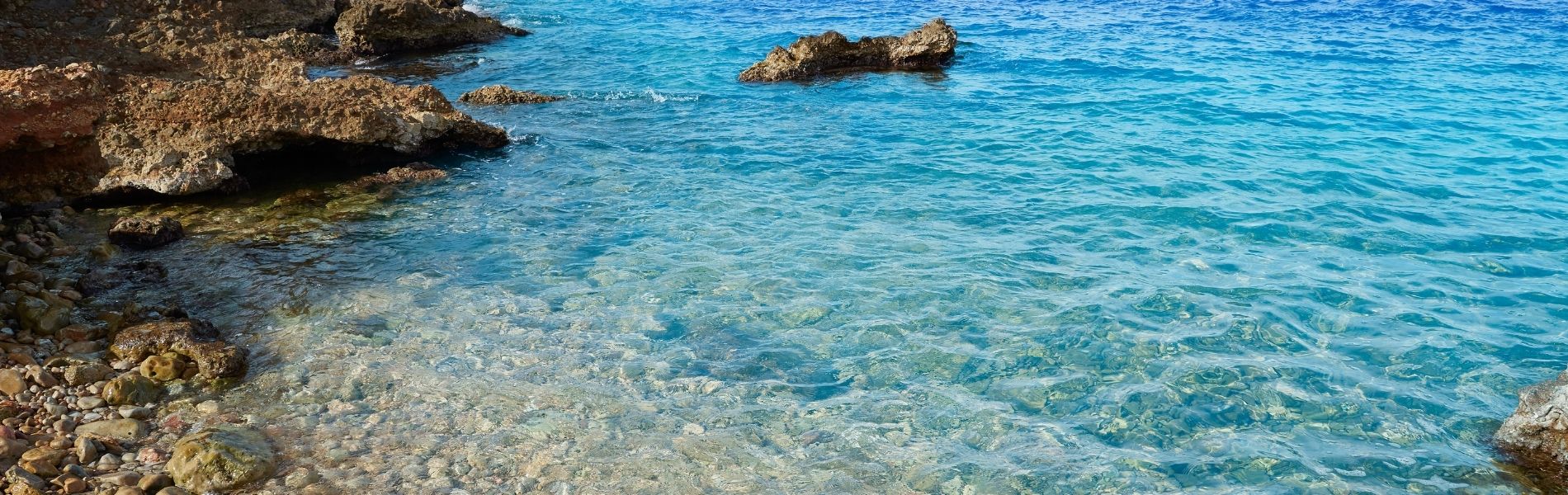 Aguas cristalinas turquesa de la costa rocosa de Dénia con piedras visibles bajo el mar transparente del Mediterráneo
