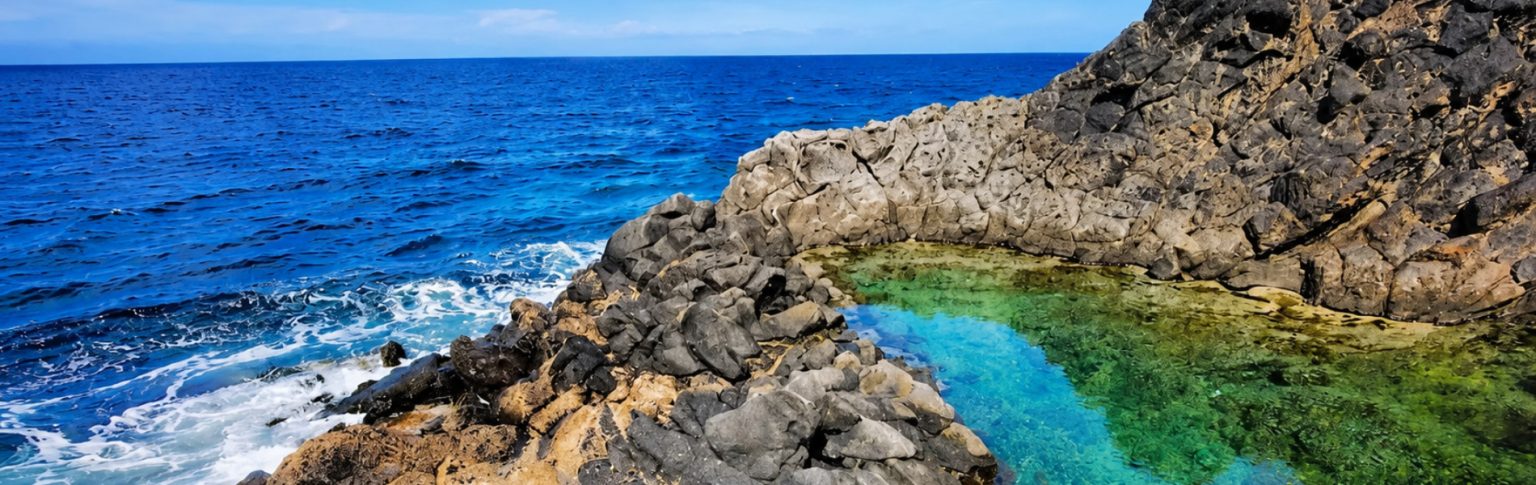 Piscina natural de roca volcánica con aguas cristalinas verdes y azules en Cala Mimar junto al mar