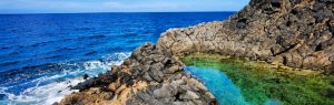 Piscina natural de roca volcánica con aguas cristalinas verdes y azules en Cala Mimar junto al mar
