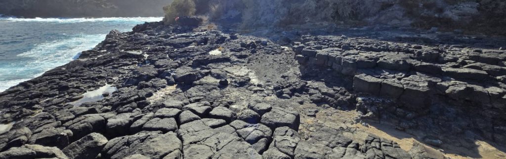 Costa rocosa volcánica de Cala Molina con formaciones de basalto negro junto al mar Mediterráneo en día soleado