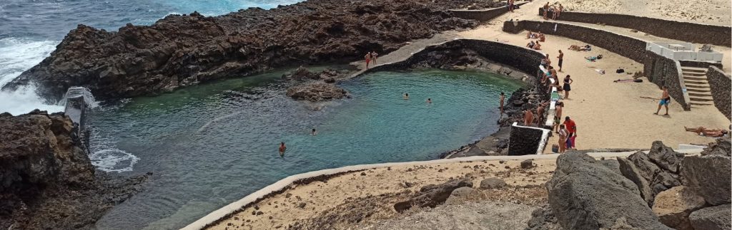 Piscina natural Los Cocoteros en Lanzarote con aguas turquesas entre rocas volcánicas y bañistas disfrutando del mar