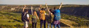 Grupo de jóvenes excursionistas con mochilas celebrando en la cima de una montaña con vistas al valle