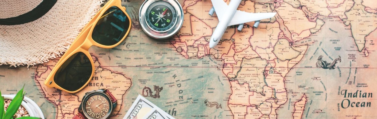 Mapa del mundo vintage con brújula, gafas de sol amarillas, avión, reloj y billetes para planificar un viaje