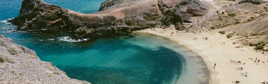 Playa Blanca en Lanzarote con aguas turquesas, arena dorada, rocas volcánicas y bañistas disfrutando del sol