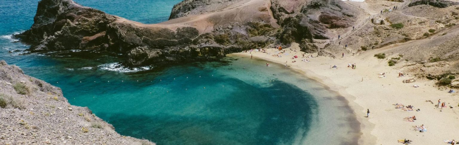 Playa Blanca en Lanzarote con aguas turquesas, arena dorada, rocas volcánicas y bañistas disfrutando del sol