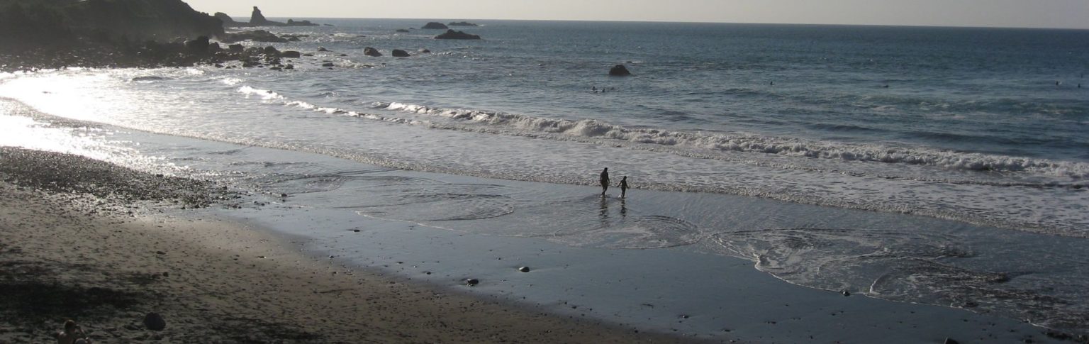 Playa de Almáciga, Tenerife, con oleaje suave, rocas volcánicas y dos personas paseando a orillas del mar