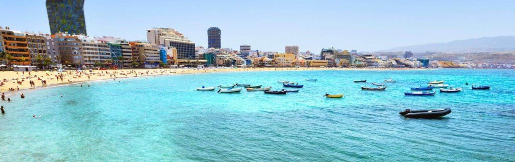Playa de Las Canteras en Las Palmas de Gran Canaria con aguas turquesas, barcas y edificios al fondo