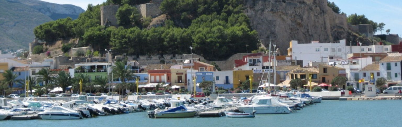 Puerto deportivo de Dénia con barcos amarrados, casas coloridas y el Castillo de Dénia sobre la roca al fondo
