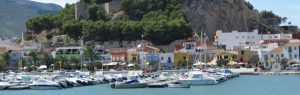 Puerto deportivo de Dénia con barcos amarrados, casas coloridas y el Castillo de Dénia sobre la roca al fondo