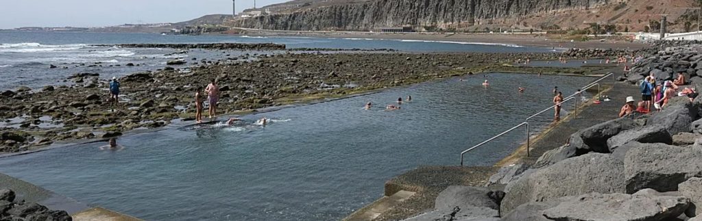 Piscinas naturales de La Laja en Gran Canaria con bañistas disfrutando del agua entre rocas volcánicas y el mar