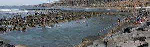 Piscinas naturales de La Laja en Gran Canaria con bañistas disfrutando del agua entre rocas volcánicas y el mar