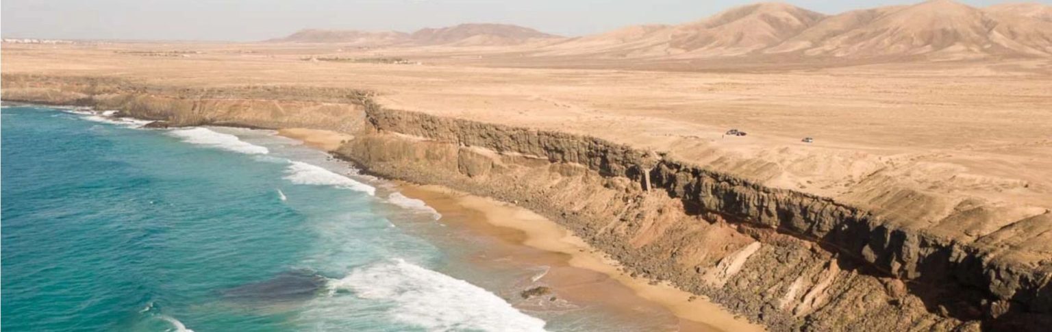 Vista aérea de la Playa de la Escalera en Fuerteventura, con acantilados volcánicos, arena dorada y mar turquesa