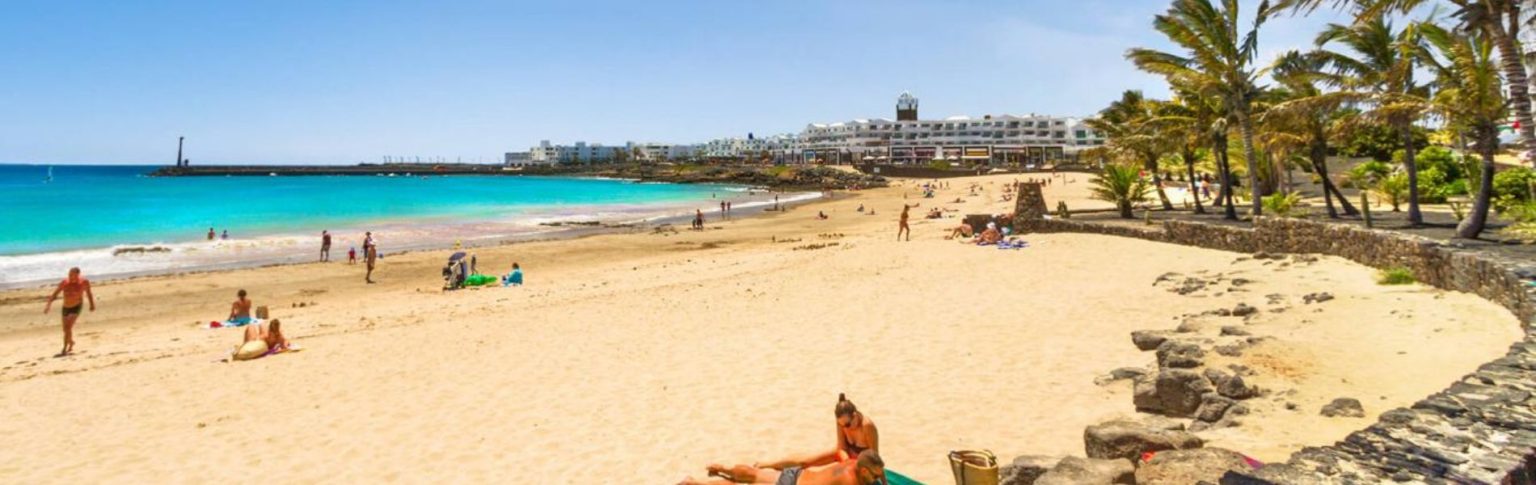 Playa de las Cucharas en Costa Teguise, Lanzarote, con arena dorada, aguas turquesas y palmeras en día soleado