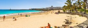 Playa de las Cucharas en Costa Teguise, Lanzarote, con arena dorada, aguas turquesas y palmeras en día soleado