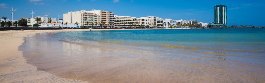 Playa del Reducto en Arrecife, Lanzarote, con aguas turquesas y el paseo marítimo al fondo en un día soleado